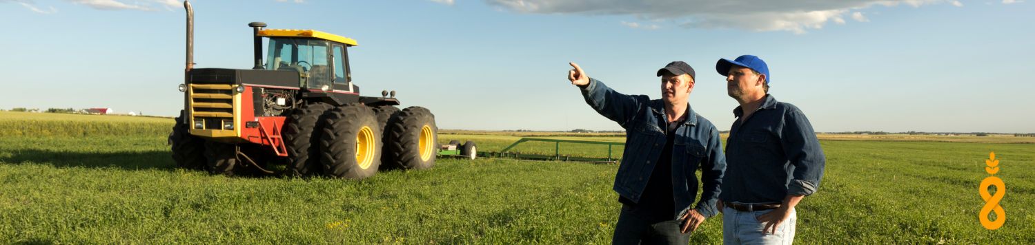 Two farmers talking in the field with a tractor in the background